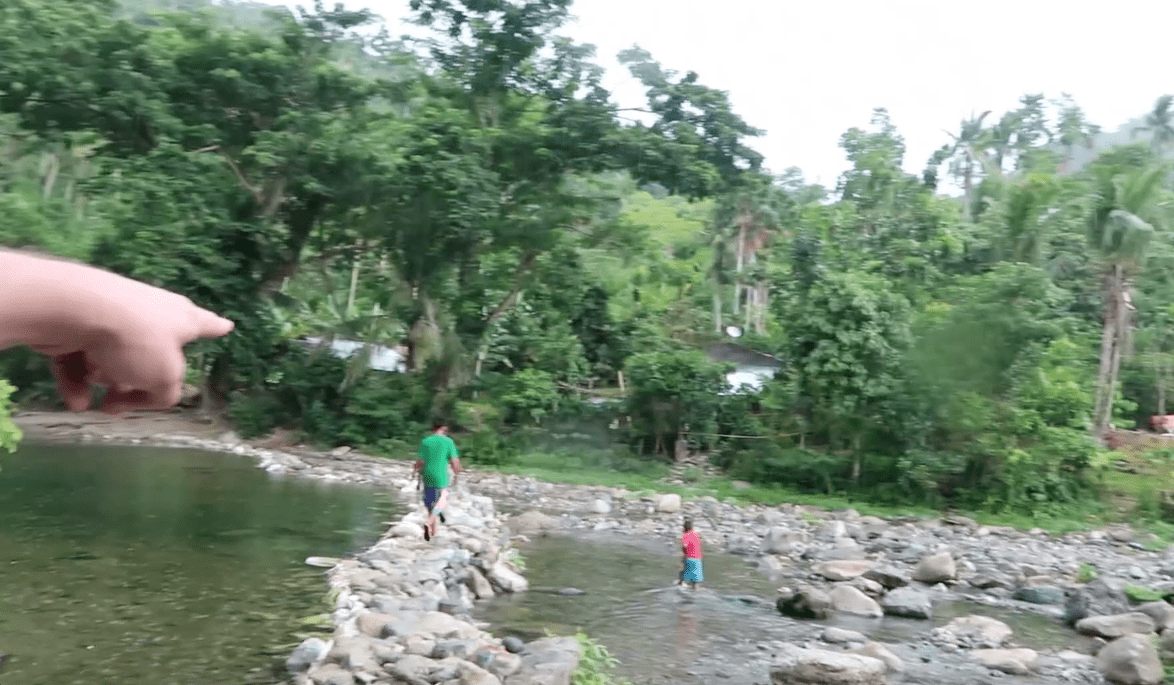pointing at filipino locals walking over rocks through river in catanduanes province philippines